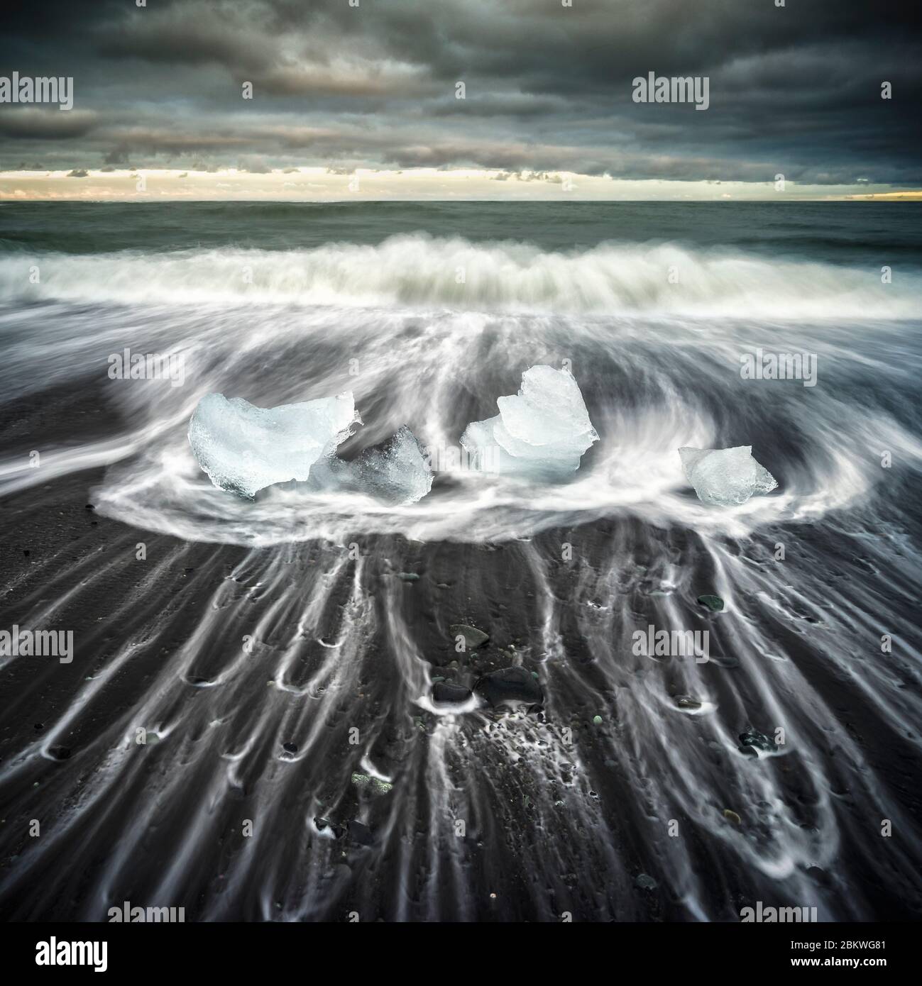 Eisberge am schwarzen Sandstrand mit Wellenstreifen um sie herum. Stockfoto