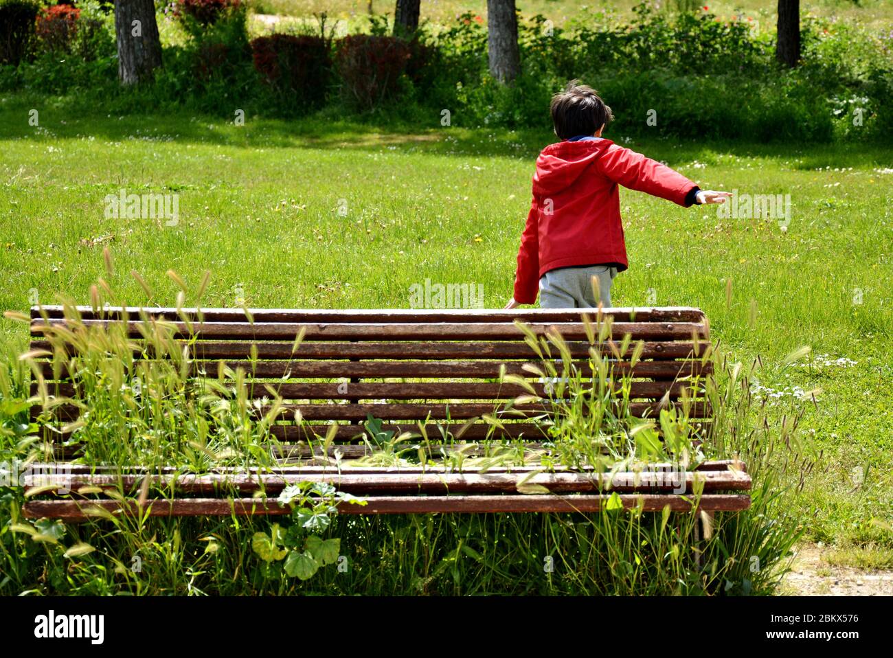 Junger Junge läuft im Park in der Nähe einer Bank voller Pflanzen Stockfoto