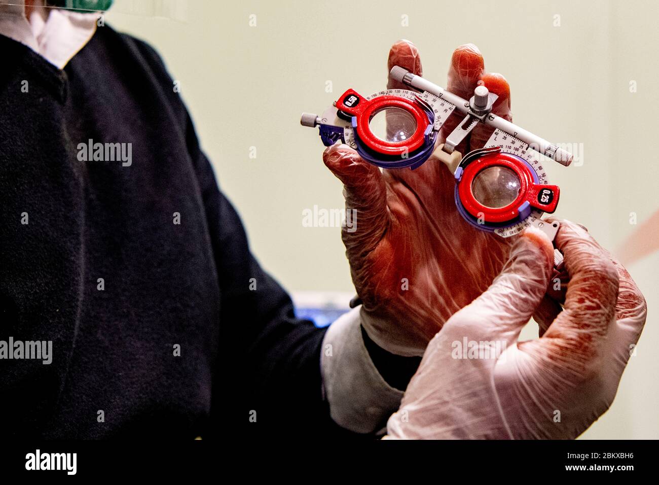 Ein Optiker, der bei der Wiedereröffnung des Unternehmens ein Plexiglas mit Handschuhen hält.durch Befolgung der Bedingungen der sozialen Distanzierung und Tragen einer Schutzmaske. Die niederländische Regierung erlaubte einigen Unternehmen, wieder zu öffnen. Stockfoto