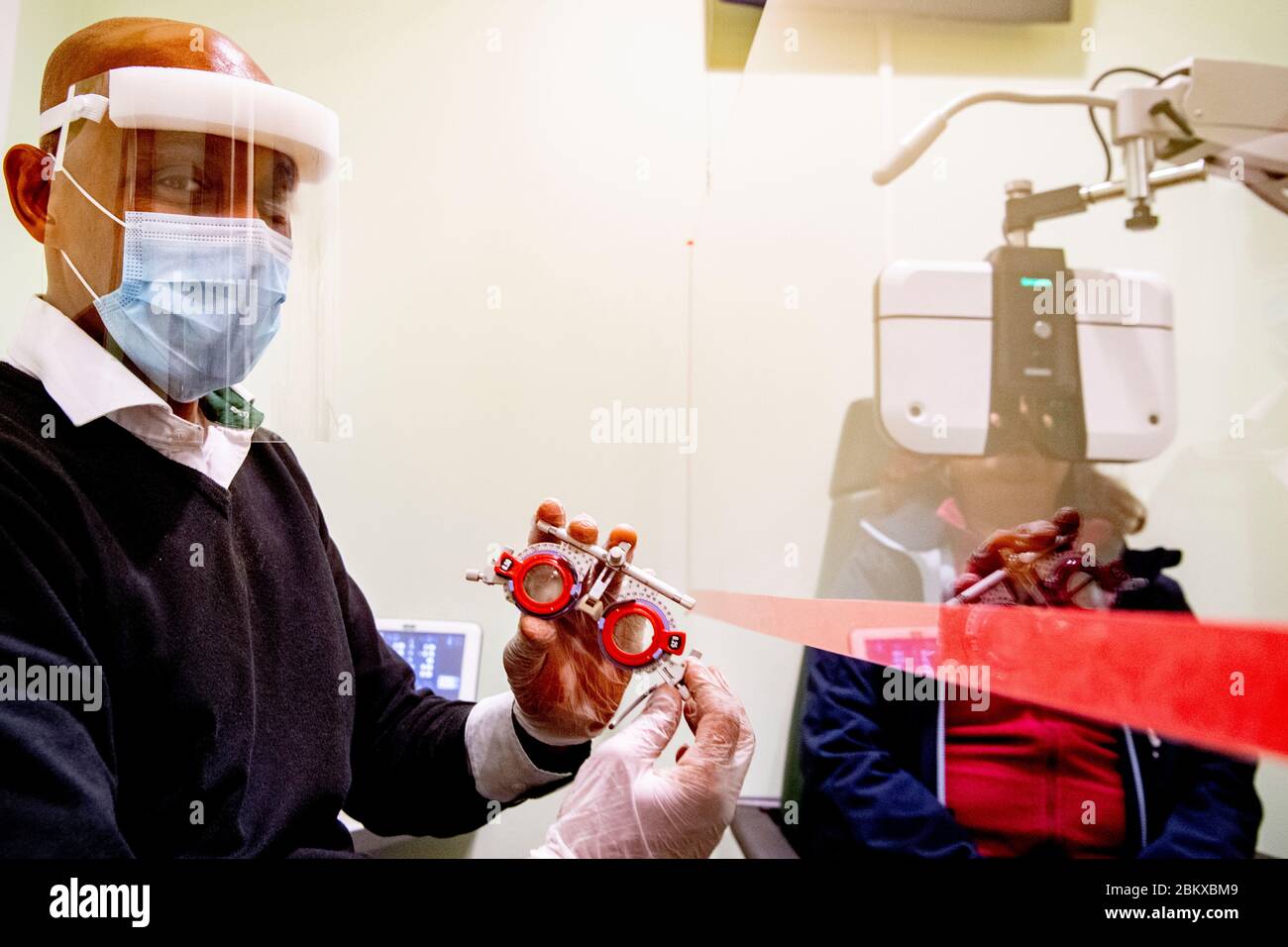 Ein Optiker, der bei der Wiedereröffnung des Unternehmens ein Plexiglas mit Handschuhen hält.durch Befolgung der Bedingungen der sozialen Distanzierung und Tragen einer Schutzmaske. Die niederländische Regierung erlaubte einigen Unternehmen, wieder zu öffnen. Stockfoto