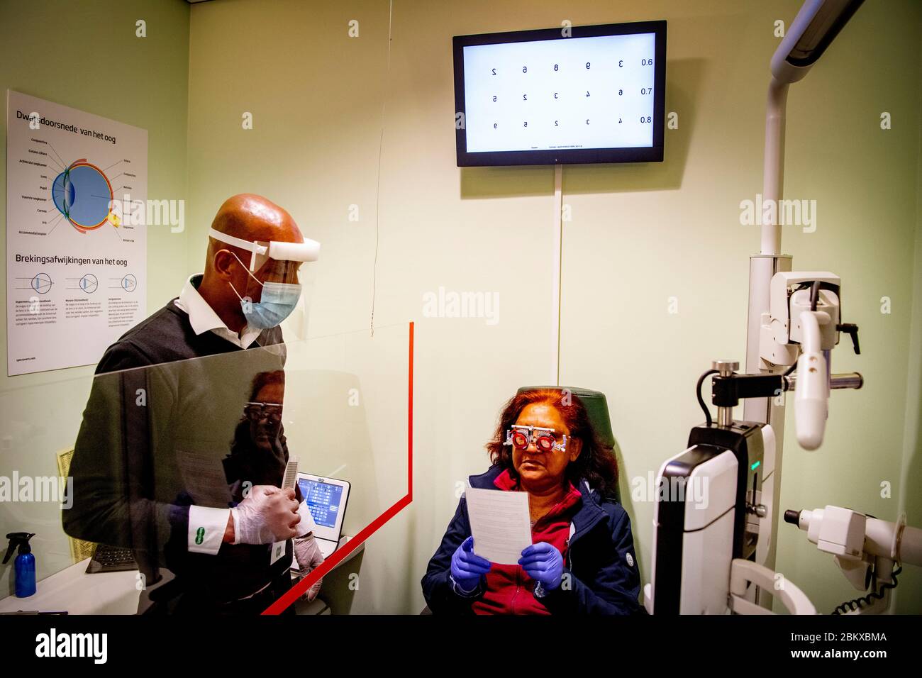 Ein Optiker, der sich bei der Wiedereröffnung eines Unternehmens vorsorglich mit Schutzschild und Maske um einen Patienten kümmerten.durch Befolgung der Bedingungen sozialer Distanzierung und Tragen einer Schutzmaske. Die niederländische Regierung erlaubte einigen Unternehmen, wieder zu öffnen. Stockfoto
