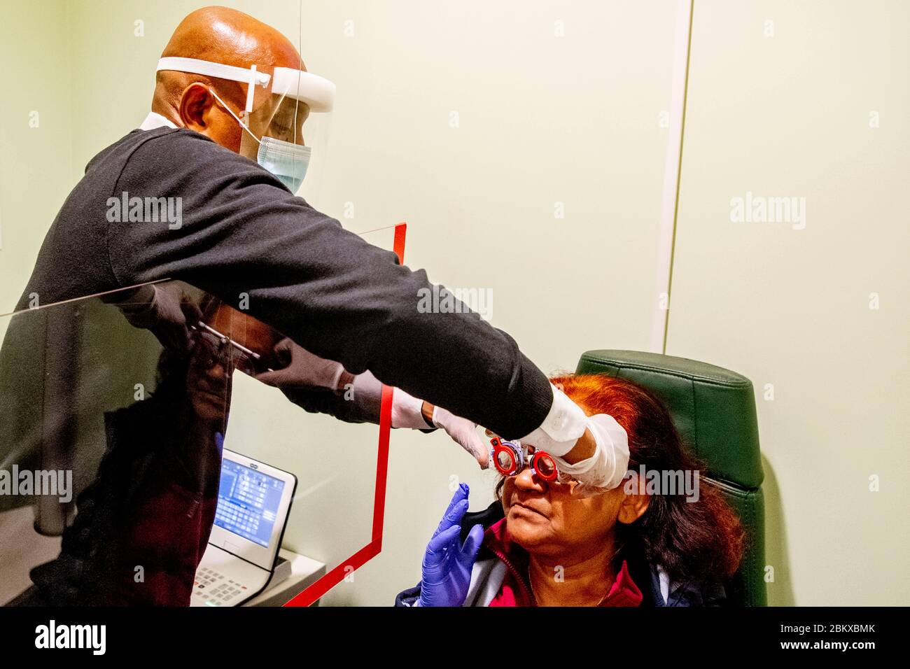 Ein Optiker, der sich bei der Wiedereröffnung eines Unternehmens vorsorglich mit Schutzschild und Maske um einen Patienten kümmerten.durch Befolgung der Bedingungen sozialer Distanzierung und Tragen einer Schutzmaske. Die niederländische Regierung erlaubte einigen Unternehmen, wieder zu öffnen. Stockfoto