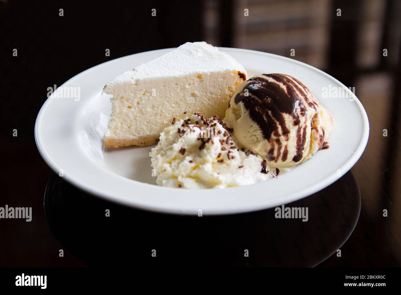 Eine Scheibe Käsekuchen mit Eis und Schlagsahne auf einem weißen Teller. Konzeptuelle Food-Fotografie mit Pflanzendekoration. Stockfoto