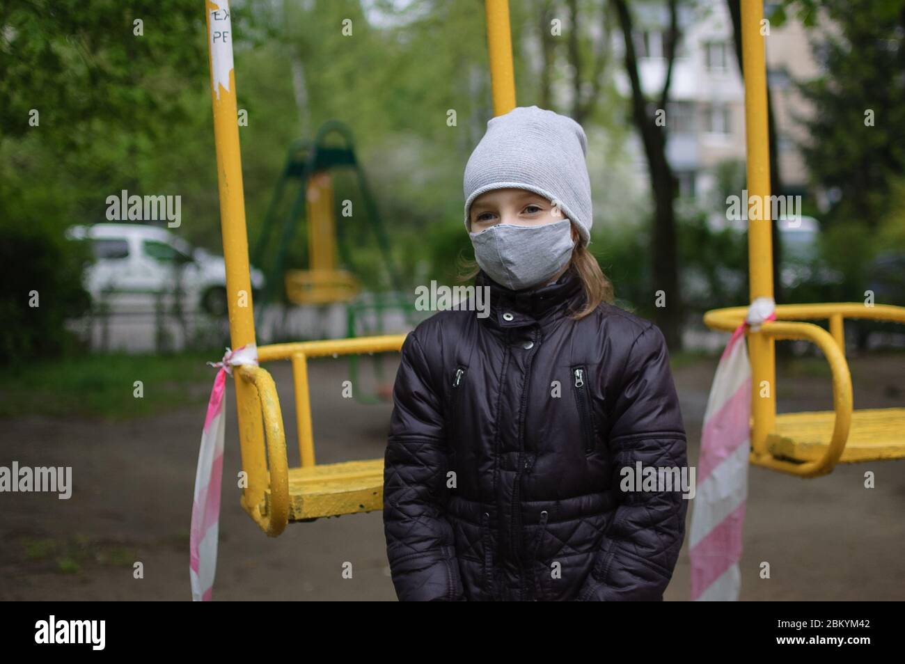 Porträt von traurigen Mädchen in grauen Gesichtsmaske und dunkle Jacke auf  geschlossenen Spielplatz im Freien. Quarantänemaßnahmen gegen COVID-19.  Coronavirus-Pandemie Stockfotografie - Alamy