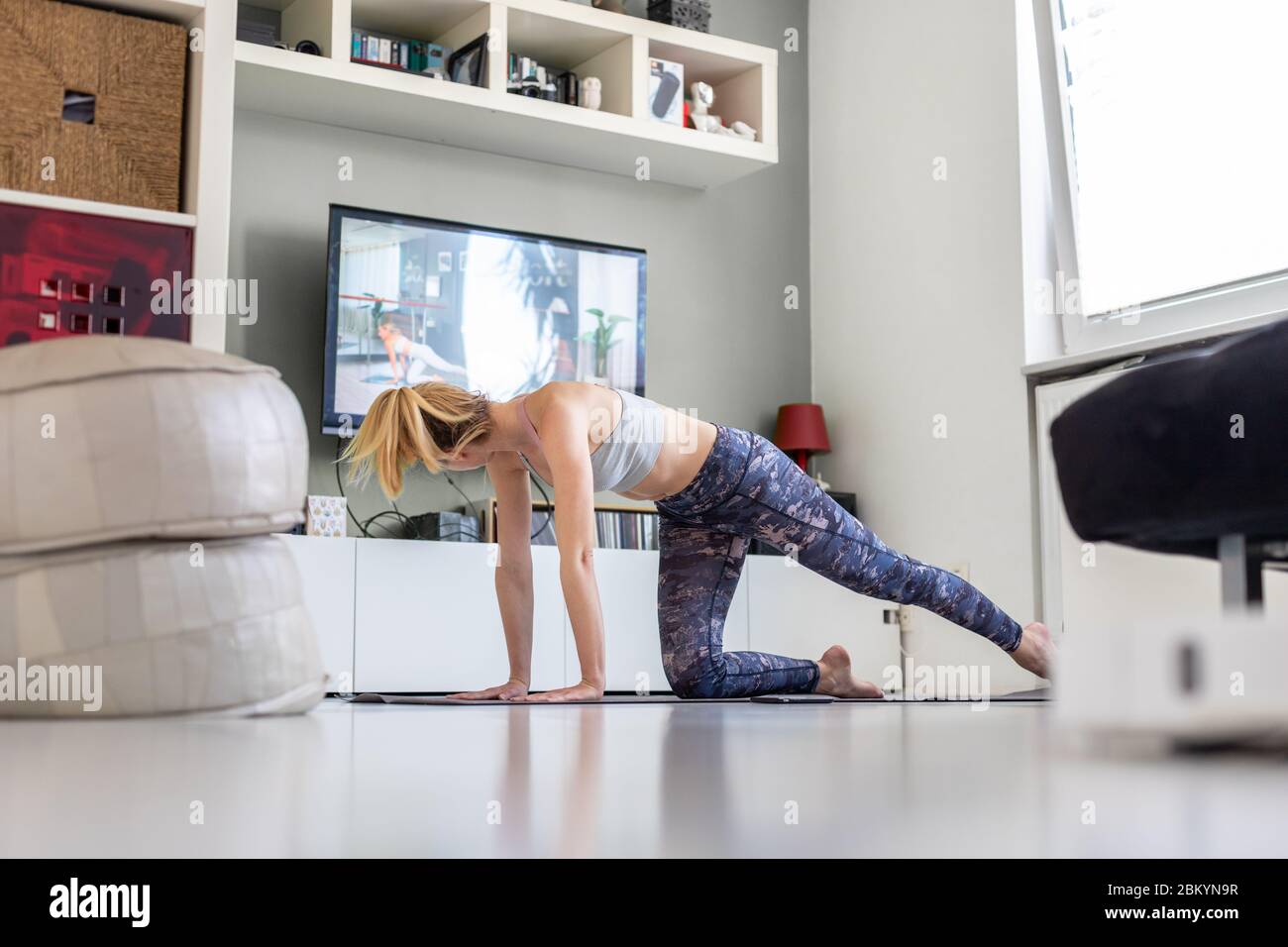 Attraktive sportliche Frau, die zu Hause arbeitet und Pilates vor dem Fernseher in ihrem Wohnzimmer Sport macht. Soziale Distanzierung. Bleiben Sie gesund und Stockfoto