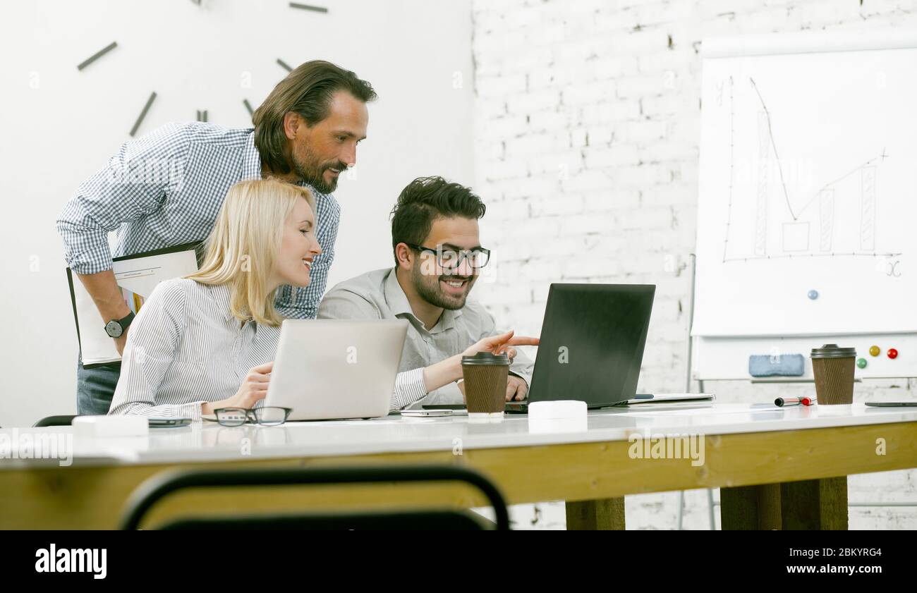 Teamarbeit von Kollegen, die gemeinsam Nachrichten auf einem Computer im Light Office lesen Stockfoto