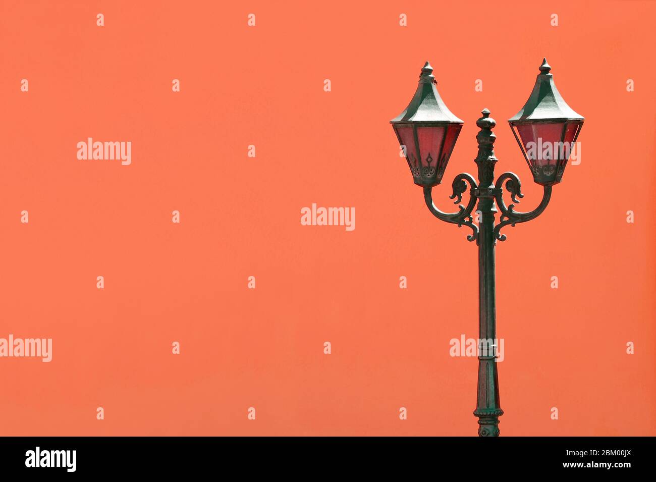 Schwarzer Vintage-Lamppost gegen leuchtend orange gefärbte Betonwand Stockfoto