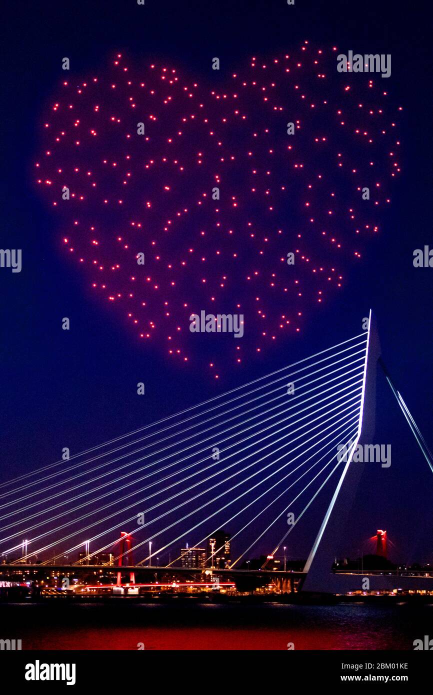 Rotterdam, Niederlande. Mai 2020. Ein Schwarm von 300 leuchtenden Drohnen,  die über der Maas auf der Erasmus-Brücke als Hommage an Freiheit und  Gesundheit fliegen, mit den niederländischen Flaggen-Farben (rot-weiß-blau)  in Herzform. Quelle: