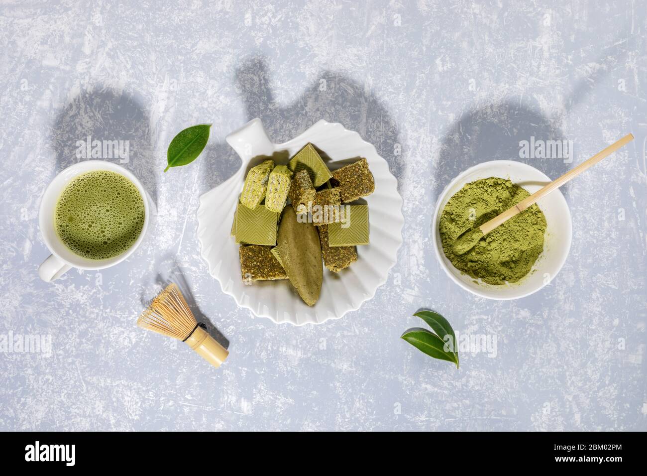 Matcha grüner Tee, Matcha Pulver, Leckereien mit Matcha, Schneebesen und Blättern auf hellgrauem Hintergrund mit Schatten. Matcha Tee und Desserts - gesund o Stockfoto