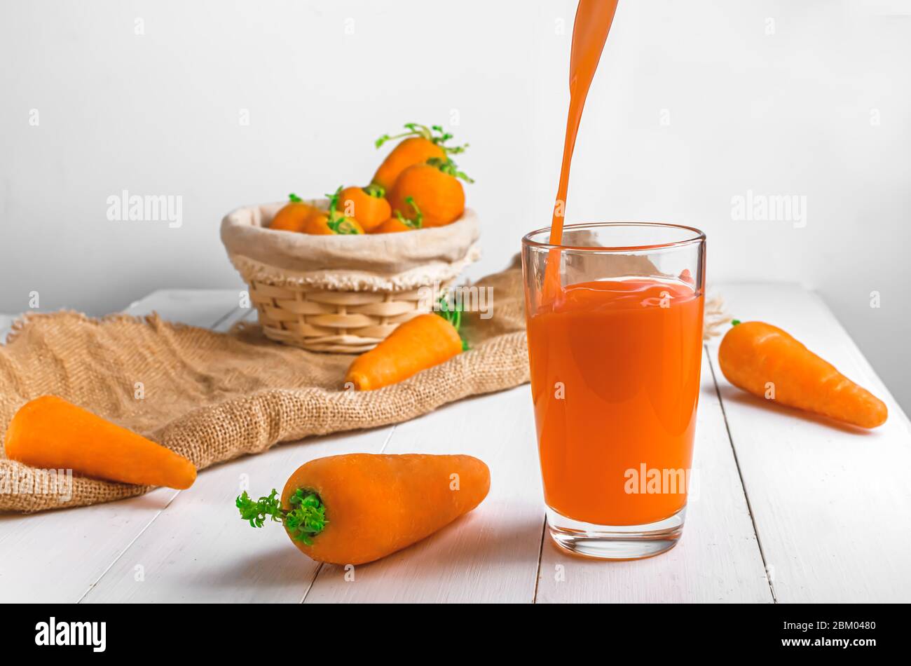 Karottensaft wird in ein transparentes Glas gegossen. Helle Sommerfotografie Stockfoto