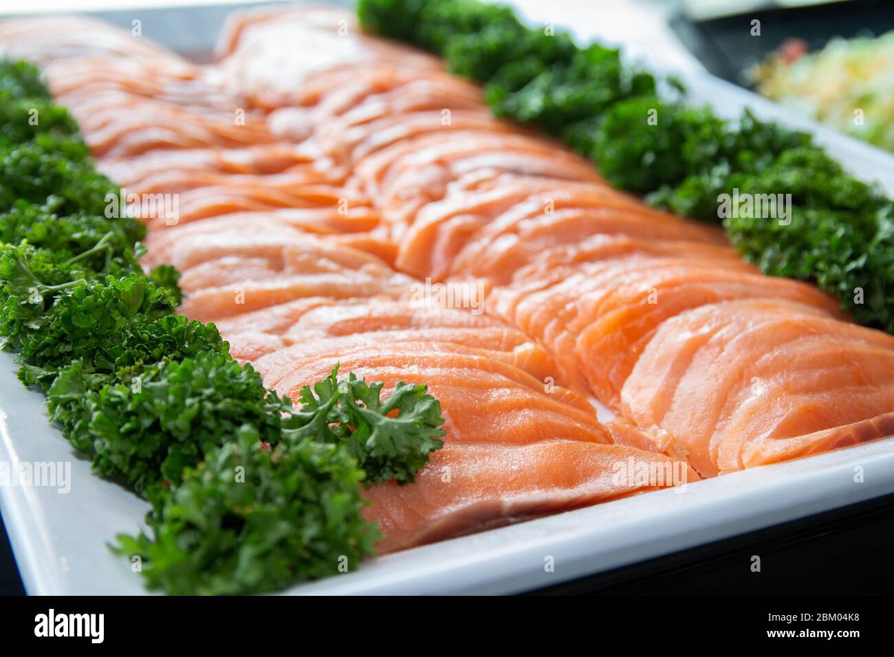 Frischer roher Lachs wird auf einem weißen Tablett mit Gemüsedekoration serviert. Stockfoto