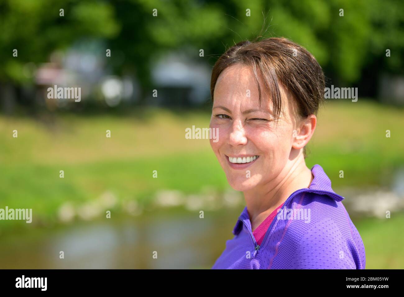 Attraktive hispanische Frau, die sich beim Joggen in der Frühlingslandschaft dreht und dabei eine Pause macht, vor der Kamera knickst Stockfoto