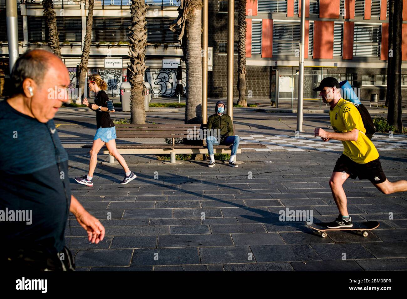 Barcelona, Spanien. Mai 2020. 6. Mai 2020, Barcelona, Katalonien, Spanien - in Barcelona sitzt ein Mann mit Gesichtsmaske früh morgens auf einer Bank, während Leute, die Sport treiben, vorbeikommen. Die Deeskalationsmaßnahmen im Rahmen des Coronavirus erlauben es den Spaniern, einige Stunden am Tag nach bestimmten Zeitplänen spazieren zu gehen oder Sport zu treiben, heute stimmt der spanische Kongress über eine neue Erweiterung des Alarmzustands ab.Jordi Boixareu/Alamy Live News Stockfoto