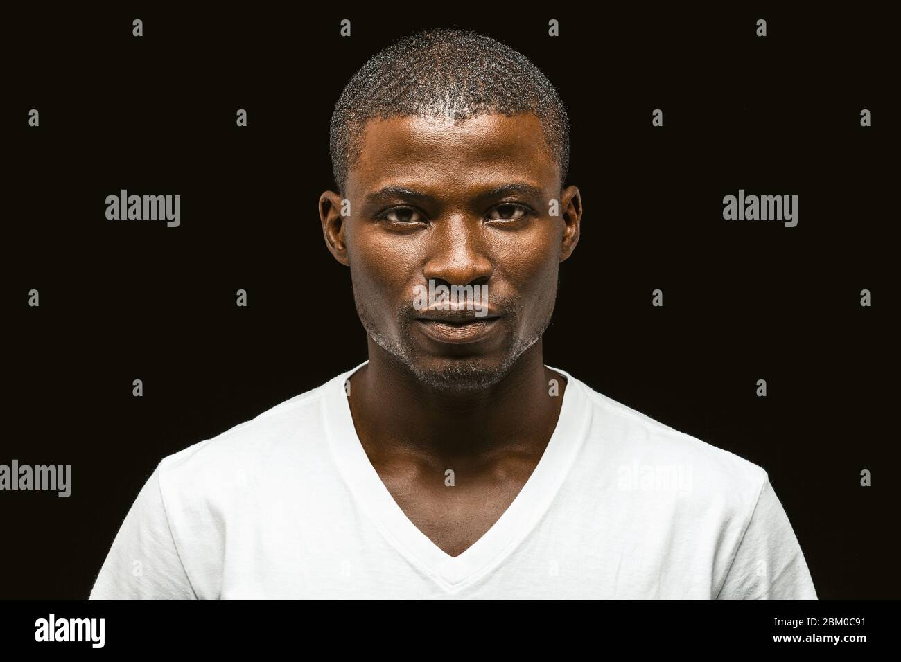 Seriöse afroamerikanische Mann, der die Kamera anschaut, attraktive dunkelhäutige junge Mann in einem weißen T-Shirt posiert, auf dem das Vertrauen isoliert zum Ausdruck kommt Stockfoto
