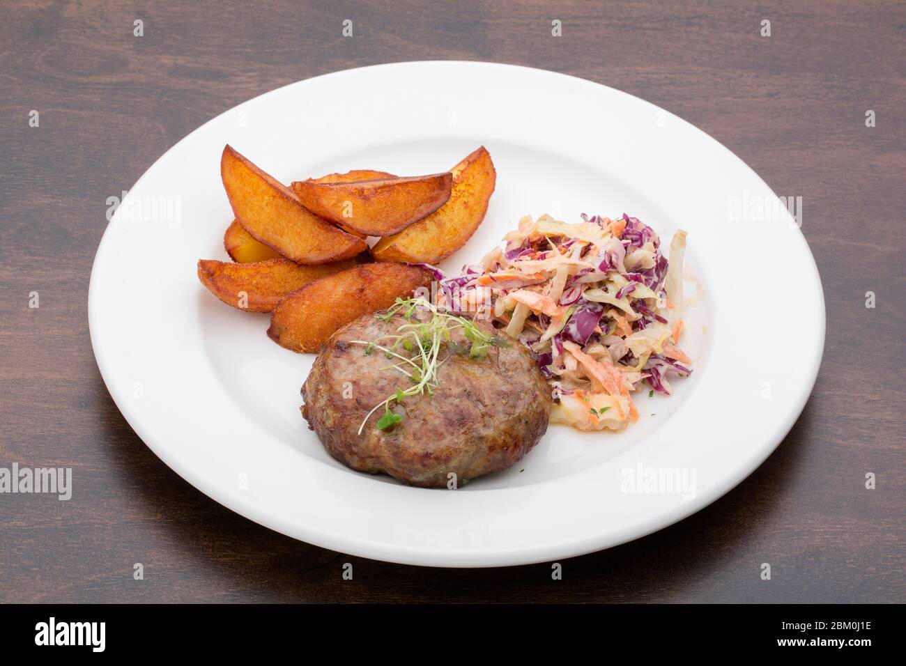 Ein Burger mit gebackenen Kartoffeln, Kohl und einem Salat in einem Keramikplatte auf einem Holztisch Stockfoto