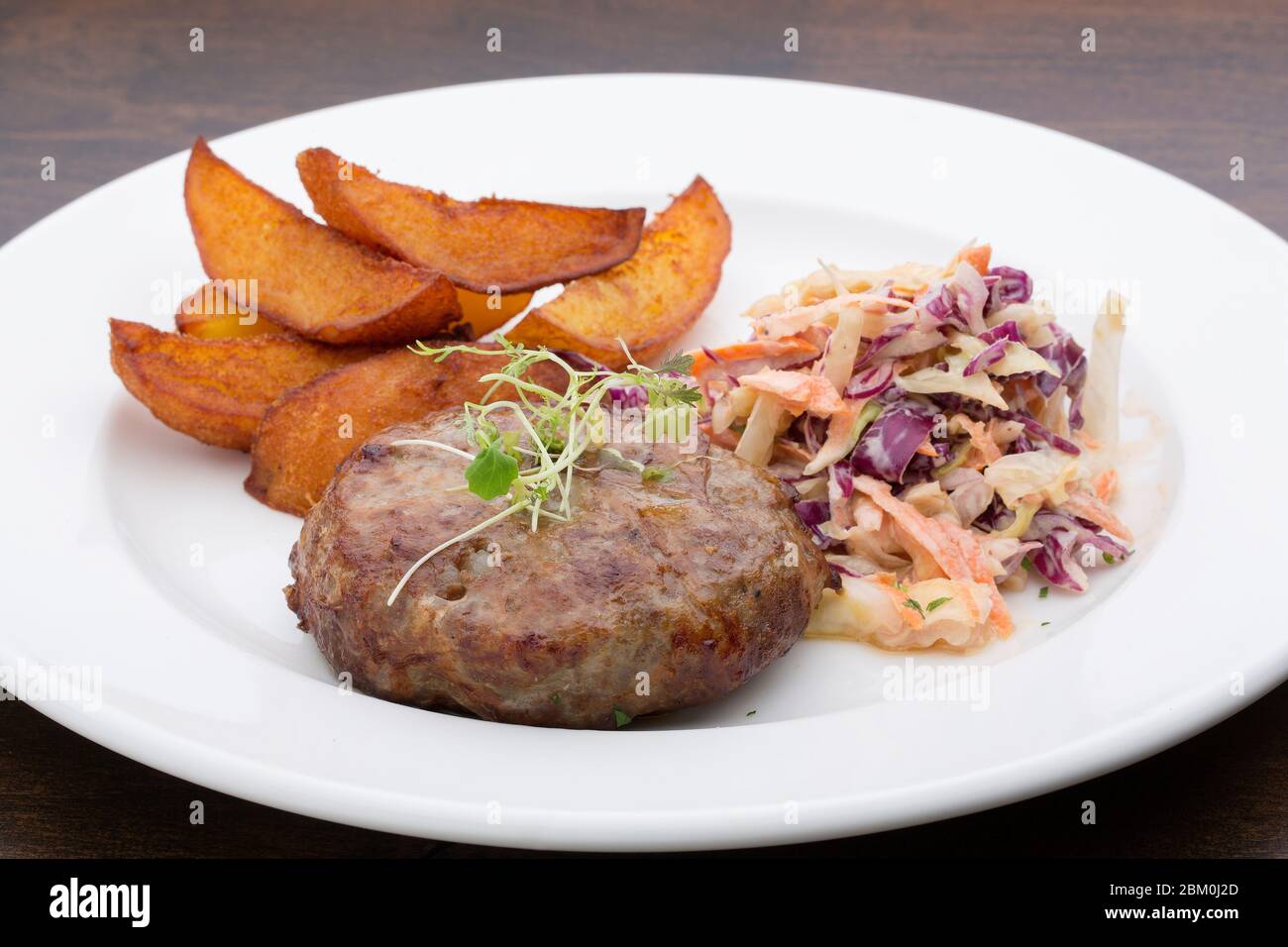 Ein Burger mit gebackenen Kartoffeln, Kohl und einem Salat in einem Keramikplatte auf einem Holztisch Stockfoto