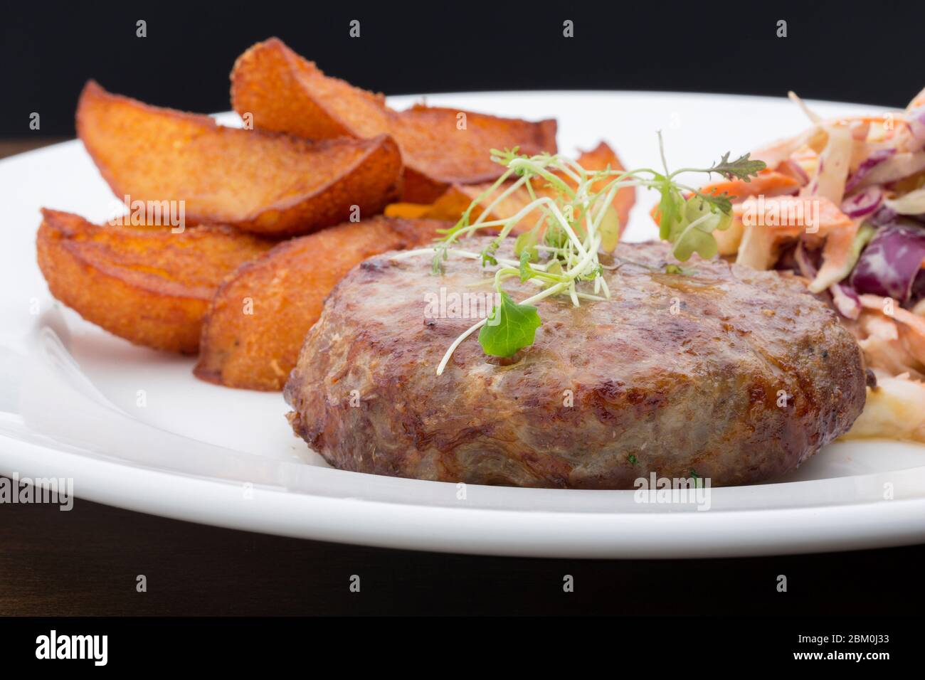 Ein Burger mit gebackenen Kartoffeln, Kohl und einem Salat in einem Keramikplatte auf einem Holztisch Stockfoto