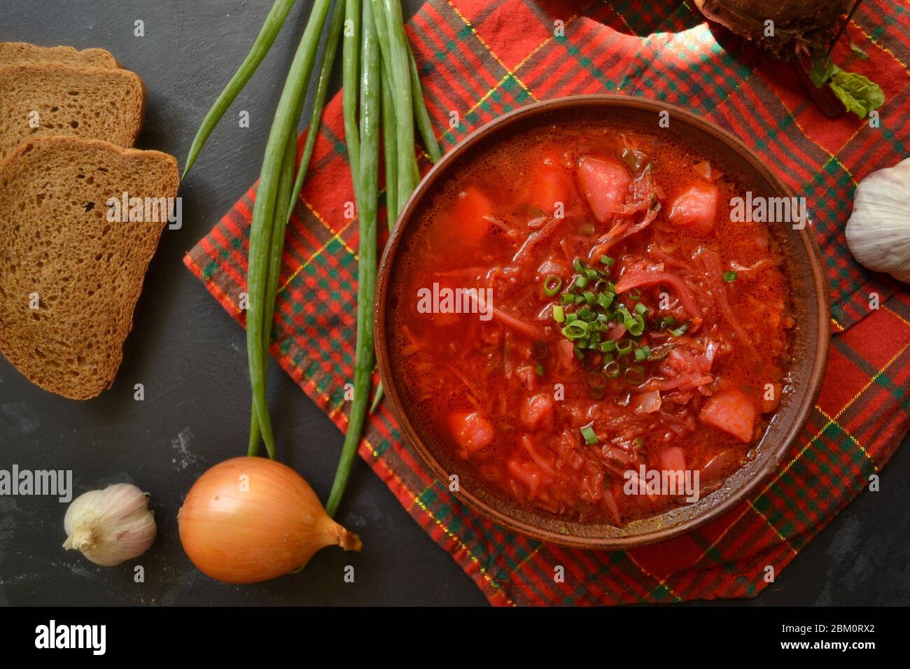 Hintergrund Essen auf dem Tisch. Ukrainische und russische Küche. Roter Borsch auf schwarzem Hintergrund. Rot kariertes Textil. Borscht mit Gemüse und Stockfoto