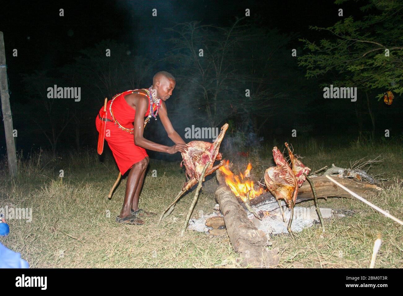 Kenia, Masai Mara, Masai (auch Maasai) Stammesmann kocht Fleisch auf offenem Feuer Stockfoto