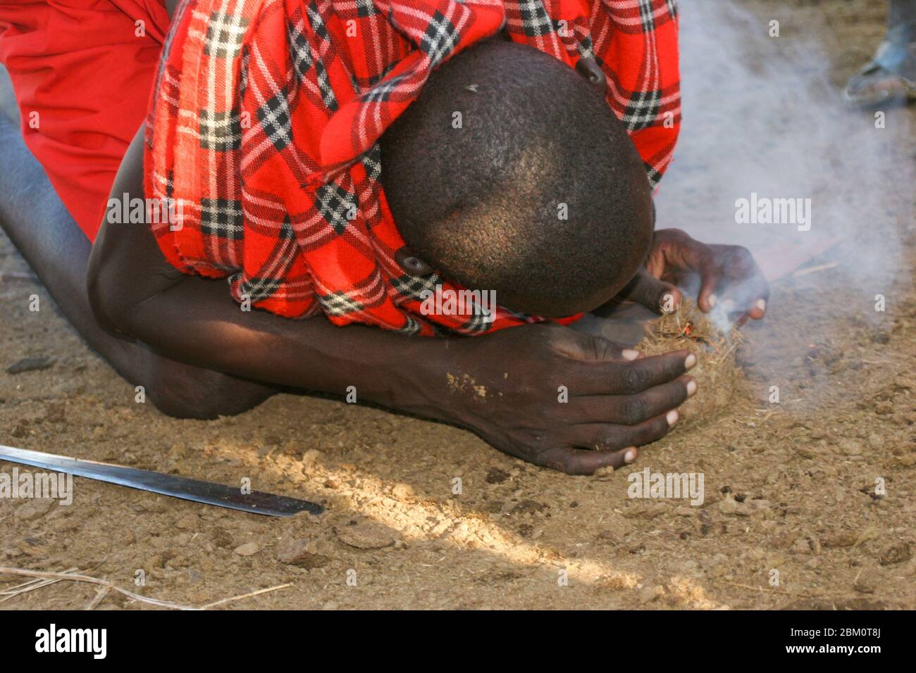 Maasai man zündet ein Feuer an, indem man zwei Stöcke reibt und auf den Zunder bläst Stockfoto