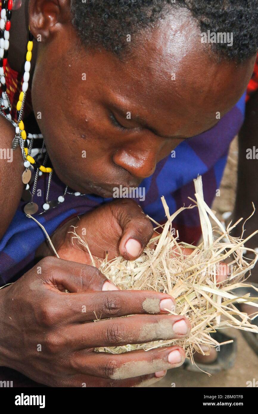 Maasai man zündet ein Feuer an, indem man zwei Stöcke reibt und auf den Zunder bläst Stockfoto