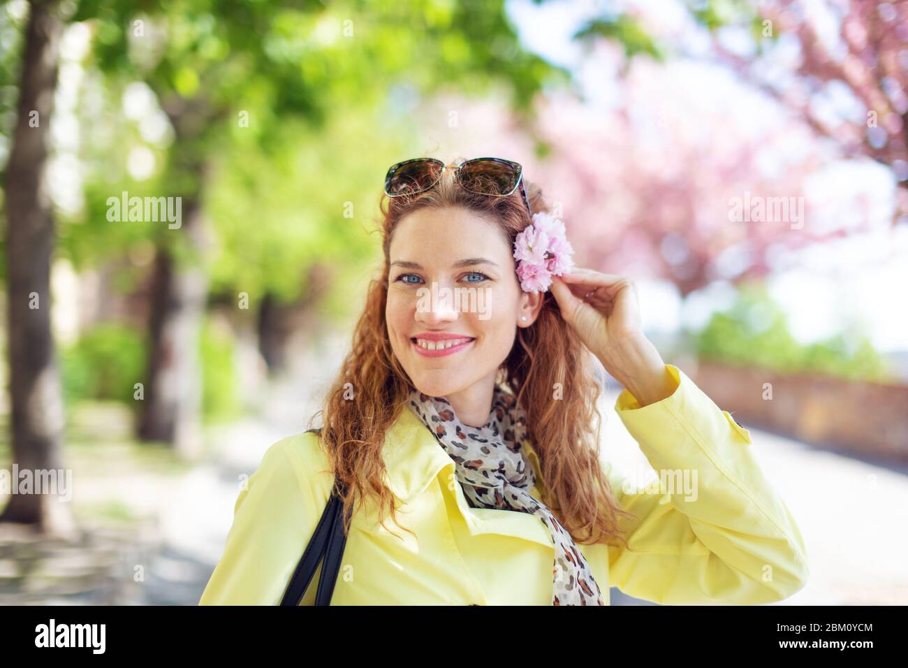 Glückliche junge Frau, die Kirschblüte im Haar im Frühling im Park, im Freien hält Stockfoto