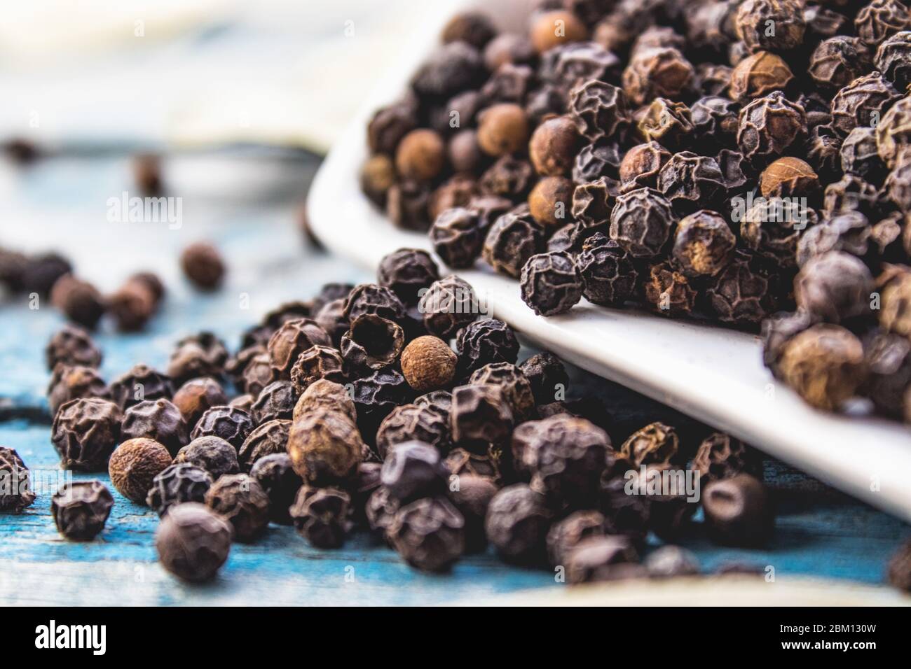 Der schwarze Pfeffer ist auf blauen Brettern verstreut. Schwarze Pfeffer Gewürze und Gewürze zum Kochen. Stockfoto