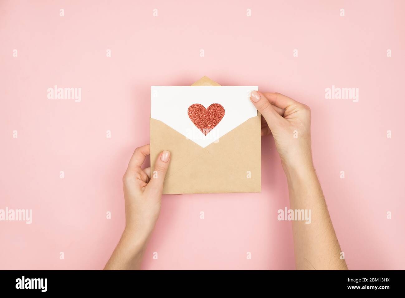 Liebesbrief in Frauenhand am Valentinstag. Handgefertigte Postkarte mit rotem Herz auf rosa Hintergrund. 14 Februar Konzept Stockfoto