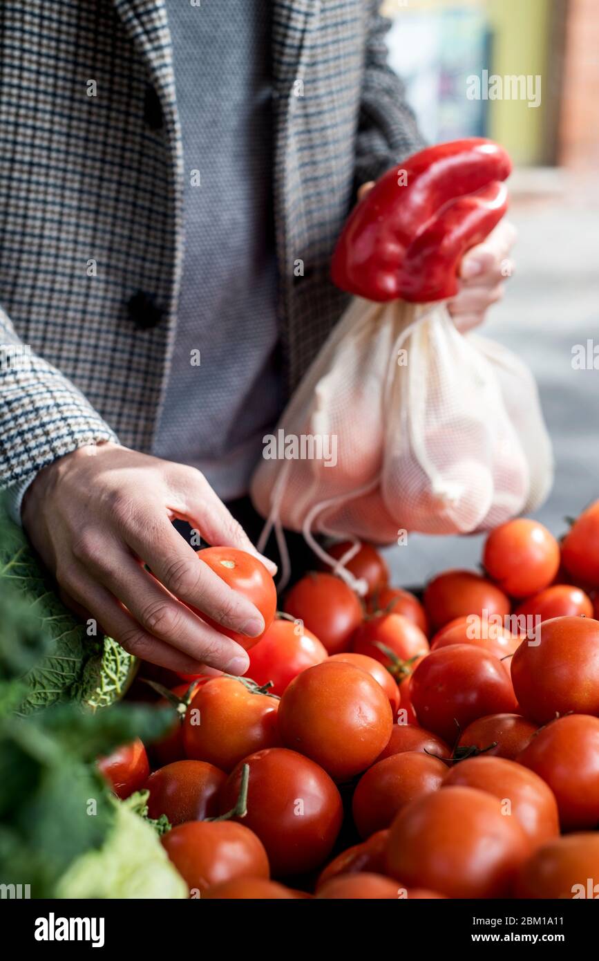 Nahaufnahme eines Mannes, der textile wiederverwendbare Netzbeutel verwendet, während er in einem Gemüsehändler einkauft, als Maßnahme zur Verringerung der Plastikverschmutzung Stockfoto