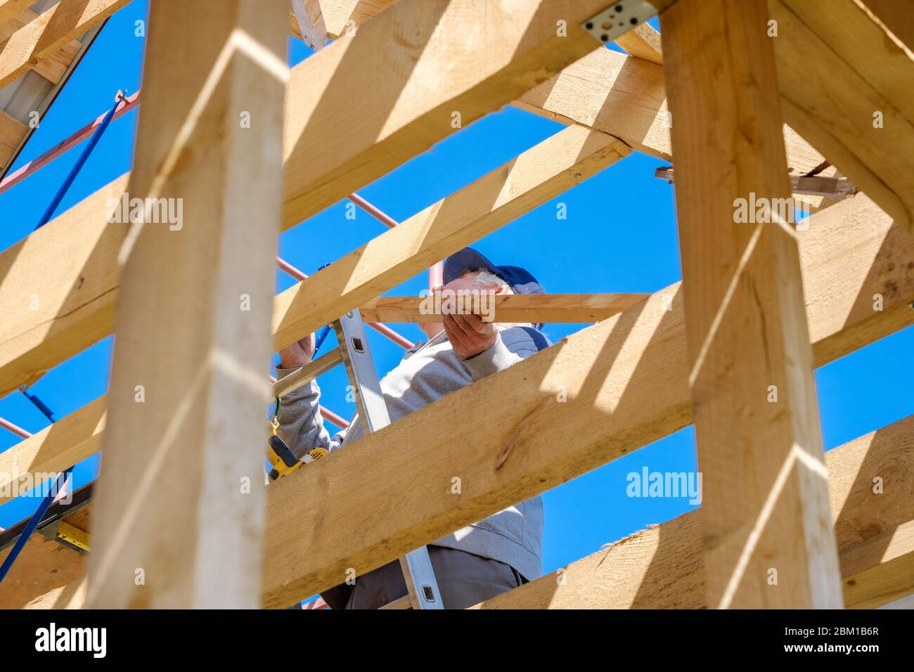 Ältere grauhaarige Baumeister sammelt den Rahmen eines hölzernen Landhaus stehend auf der Treppe gegen den blauen Himmel. Die körperliche Aktivität der elde Stockfoto