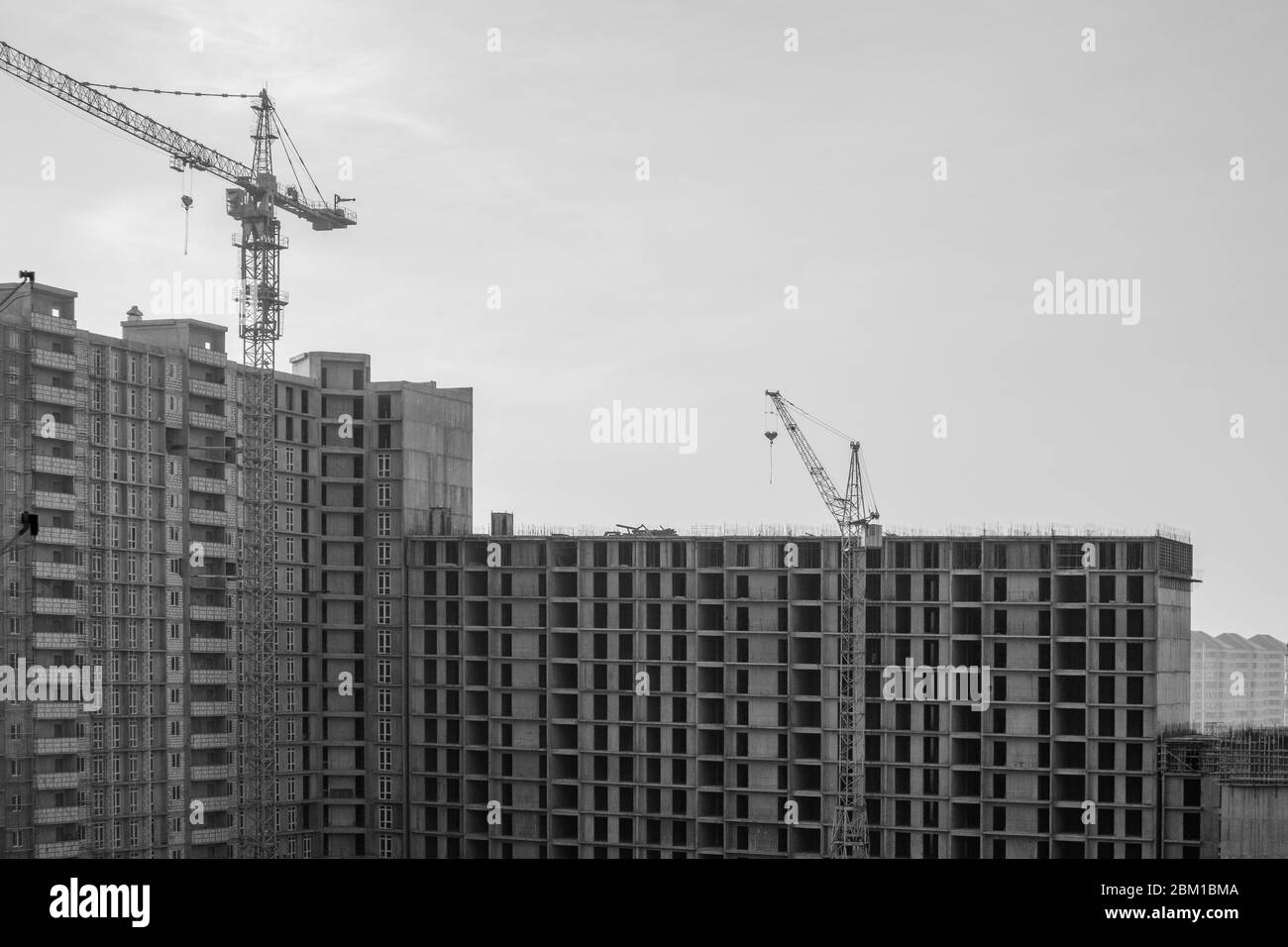 Bau eines großen Hochhauses mit Kranen mit grauem Himmel Hintergrund. Schwarz und Weiß. Stockfoto