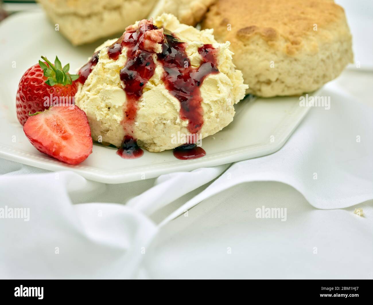 Britischer Sahnetee, Scones mit gerinnter Sahne, Erdbeermarmelade und Erdbeeren auf weißem Hintergrund, Food Stillleben Stockfoto