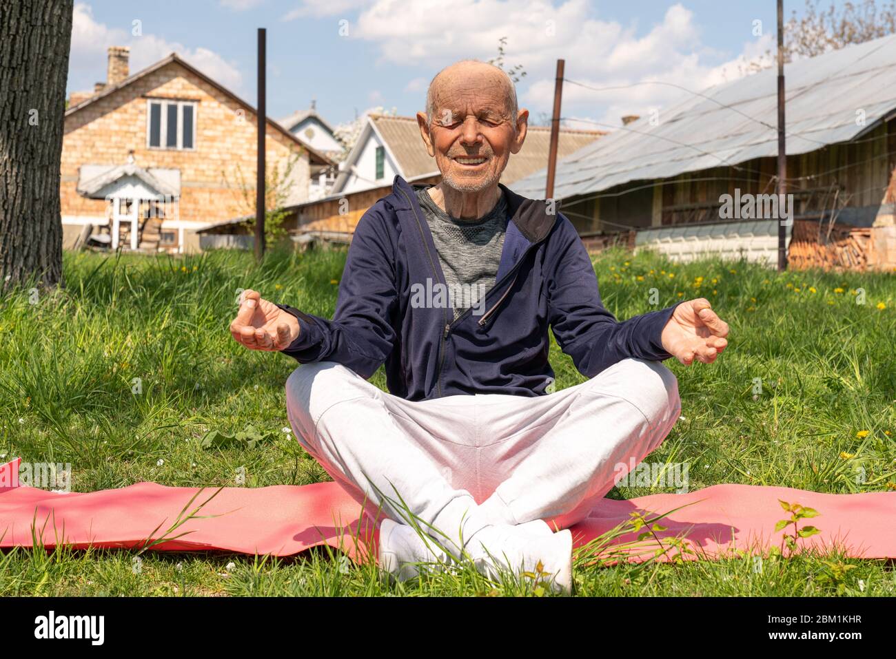 Fröhliche Männer im Alter sitzen in Lotusposition auf Yoga-Matte im Hinterhof. Aktives Sport-Workout für alte Menschen. Stockfoto