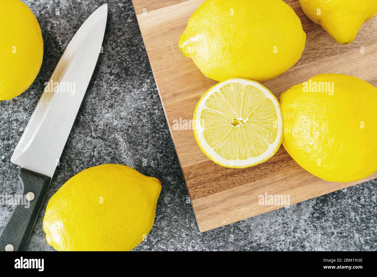 Direkt über Ansicht von reifen Bio-Zitronen auf Küchentheke mit Holzschneidebrett und Messer Stockfoto