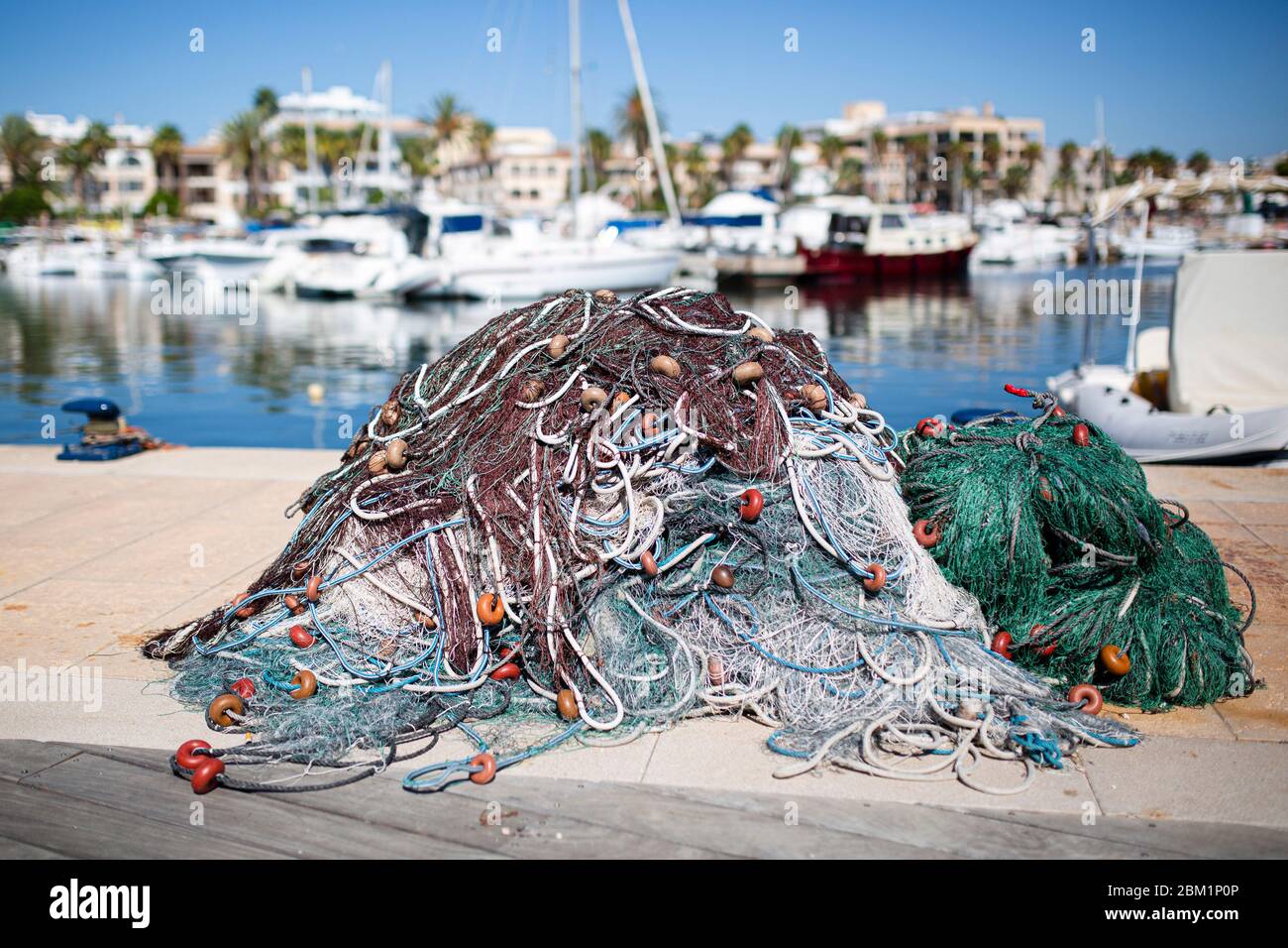 Haufen von Fischern´s Fischernetze auf einem Pier in einem Hafen. Boote und mediterrane Häuser im Hintergrund. Stockfoto