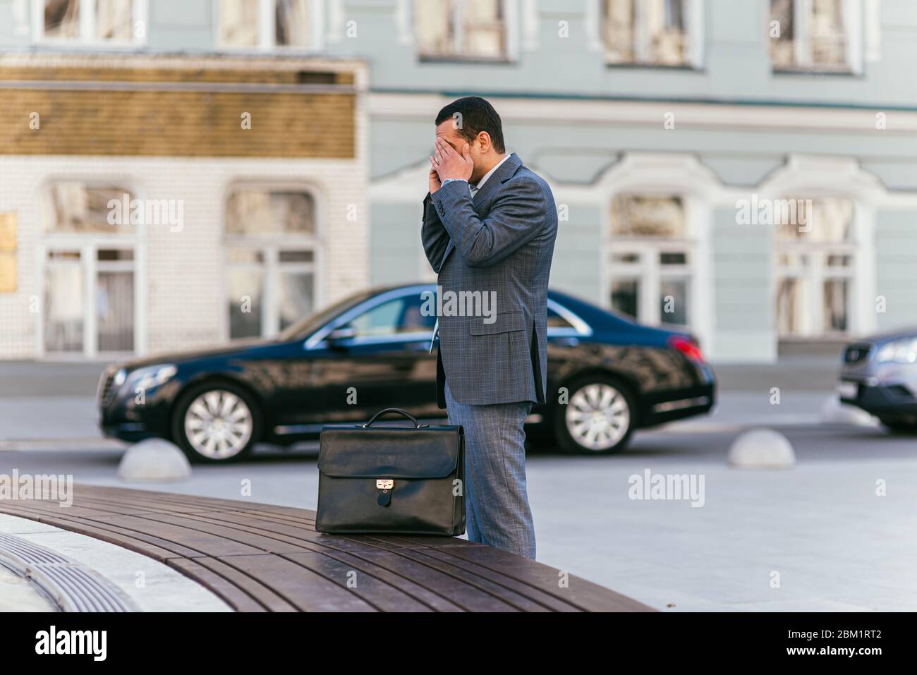 Moskau, Russland - 28. MAI 2018: Müde Geschäftsmann in einem klassischen grauen Anzug mit einer Leder-Aktentasche, die sein Gesicht umklammert und am Telefon gegen Stockfoto