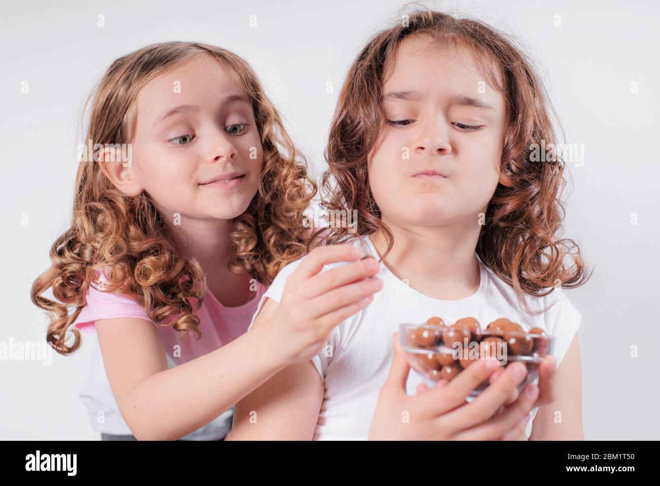 Kinder und Schokolade.zwei fröhliche Mädchen essen Schokolade auf einem hellen Hintergrund. Stockfoto