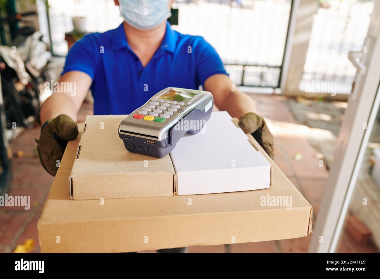 Lieferung Mann in medizinischen Maske und Handschuhe geben Pappkartons mit Pizza und Zahlungsterminal an den Kunden Stockfoto