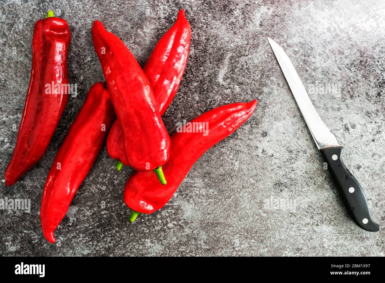 Direkt über Ansicht von roten Paprika und Schneidmesser auf Steinküchenplatte Stockfoto