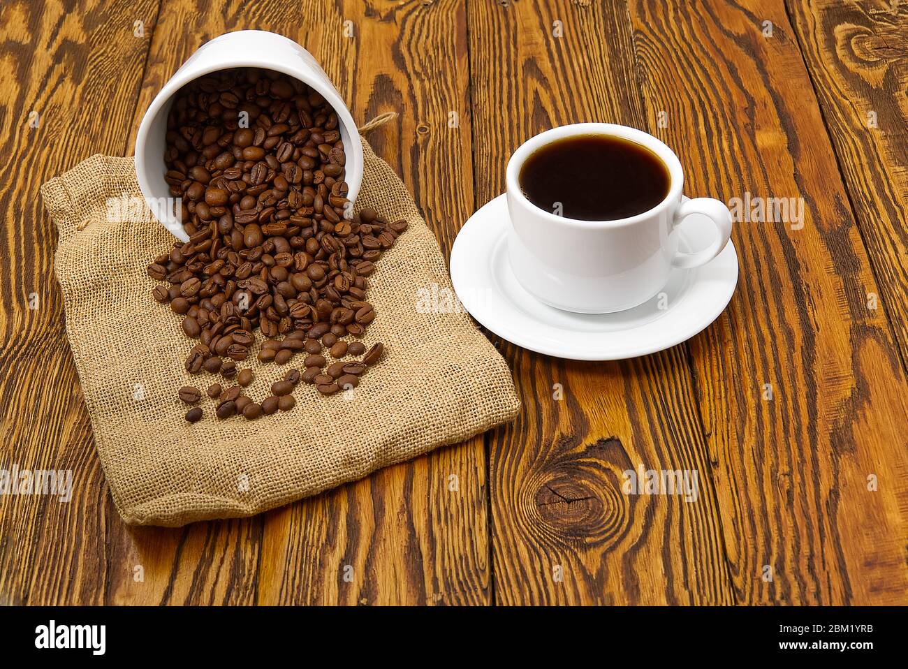Weiße Kaffeetasse mit aromatischem Kaffeegetränk auf braunem Holztisch. Kaffeesamen auf antikem Holztisch mit Tasse Kaffee Getränk Stockfoto