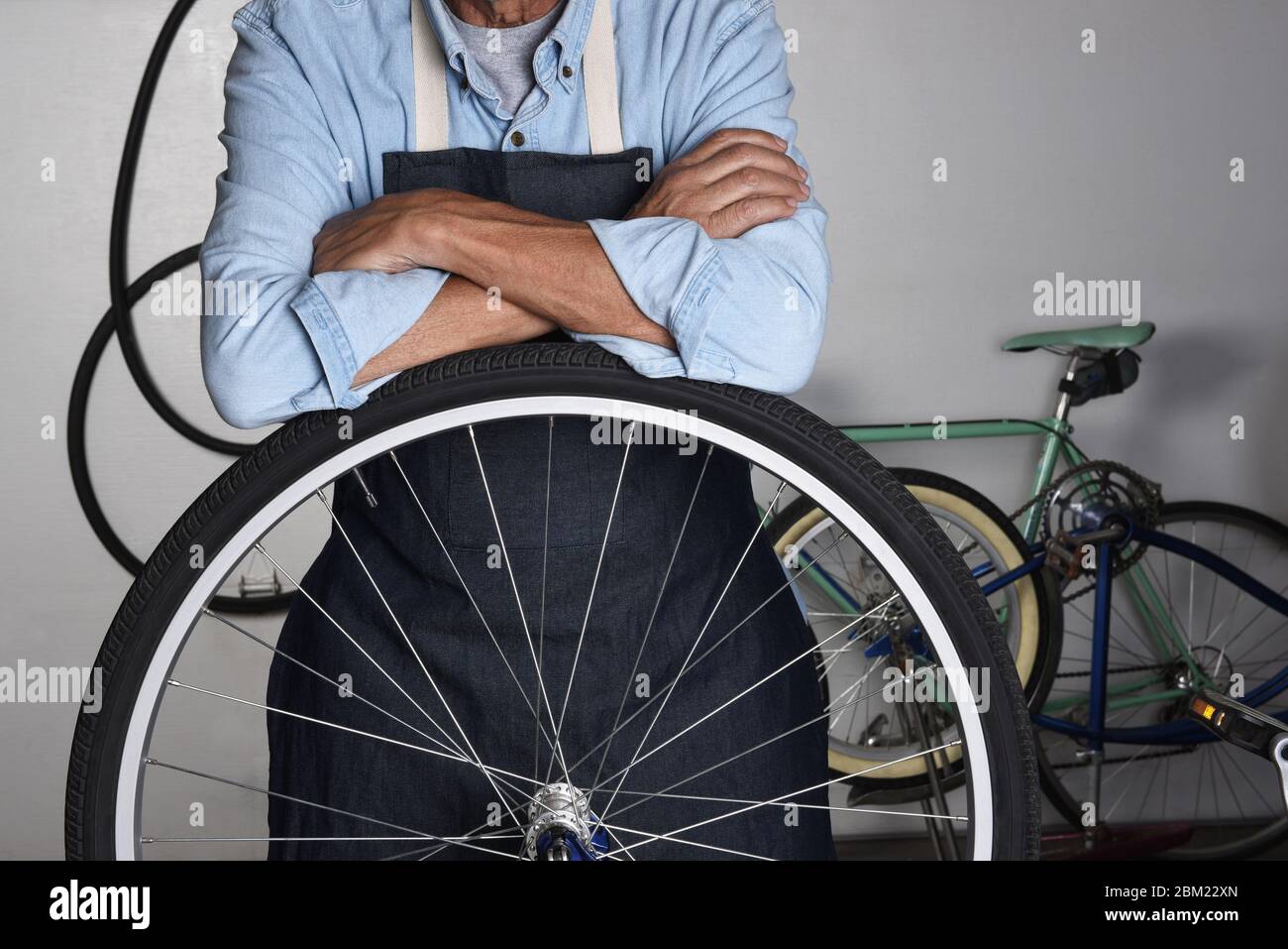 Ein Fahrradreparaturmann steht hinter dem Rad eines Fahrrads in seinem Laden. Der Mensch ist mit gefalteten Armen nicht erkennbar. Stockfoto