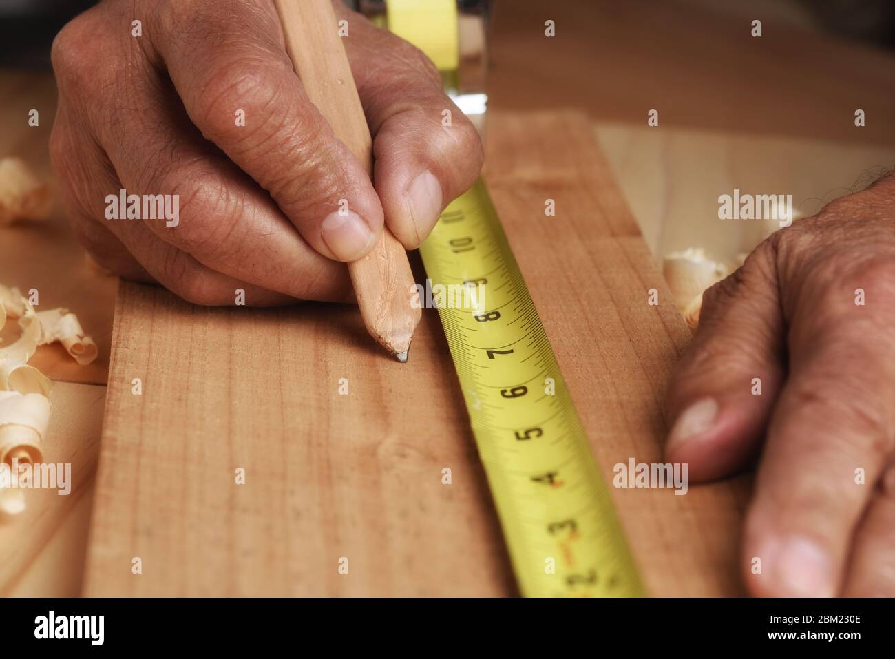 Die Nahaufnahme des Zimmermanns, der die Markierung des Brettes für das Schneiden misst. Der Mensch ist nicht erkennbar, nur Hände. Stockfoto