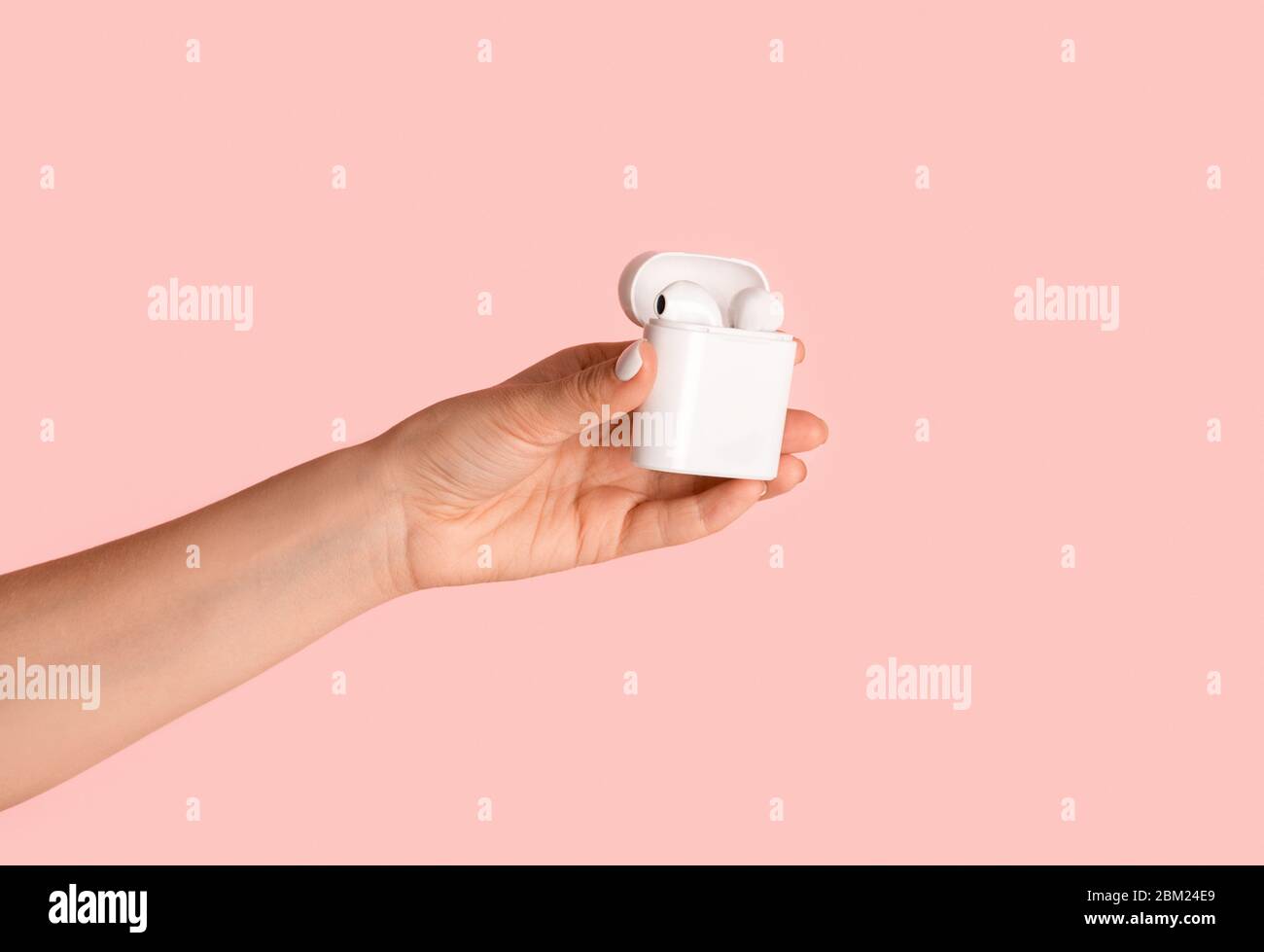Millennial Mädchen zeigt Box mit modernen Ohrstöpseln auf rosa Hintergrund, Nahaufnahme der Hand Stockfoto
