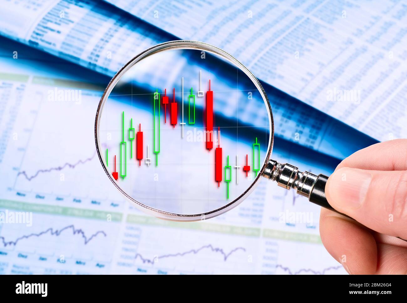 Die Lupe zeigt einen Aktienkurs als Candlestick Chart. Preistabellen und -Diagramme werden im Hintergrund angezeigt. Stockfoto