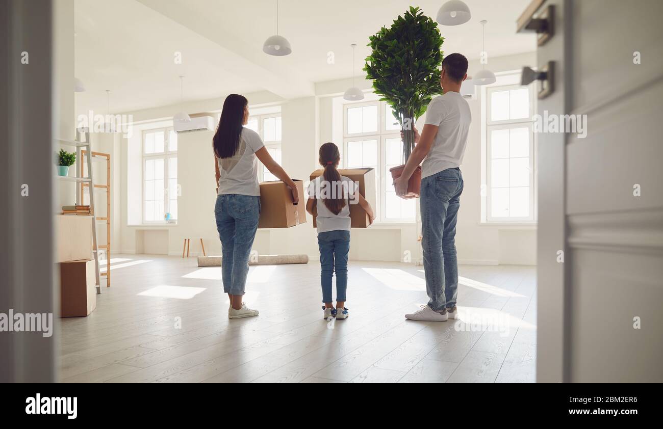 Lächelnde Familie lacht, während sie in einem sonnigen neuen Haus steht.Rückansicht. Das Konzept des Umzugsgutes neues Wohnhaus Umzug Haus Verkauf Immobilie Stockfoto