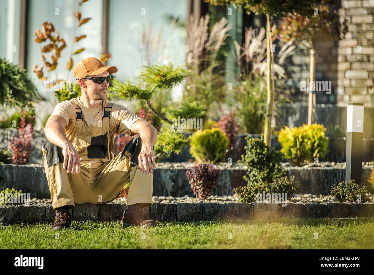 Mitte der 30er Jahre männlicher Gärtner sitzt und entspannt auf Steinkante in Wohngebiet Backard. Stockfoto