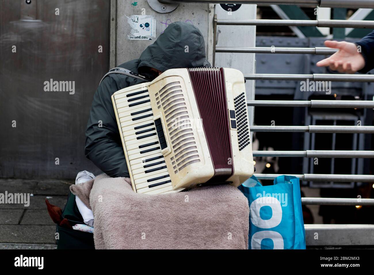 London, UK - 23. Februar 2020 unkenntlich gebeugt sich der rumänische Straßenmusiker während der Ruhepause den Kopf auf einer Ziehharmonika Stockfoto