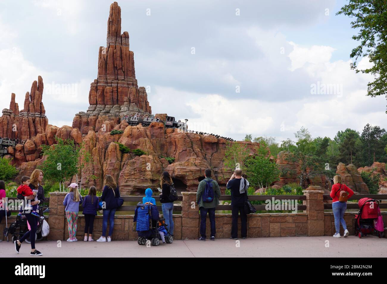 Stehen mit anderen Besuchern auf einer Straße eines Themenparks wilden Westen vor einem hohen Felsen in Frankreich. Dampflokomotive für den Personenverkehr auf bri Stockfoto