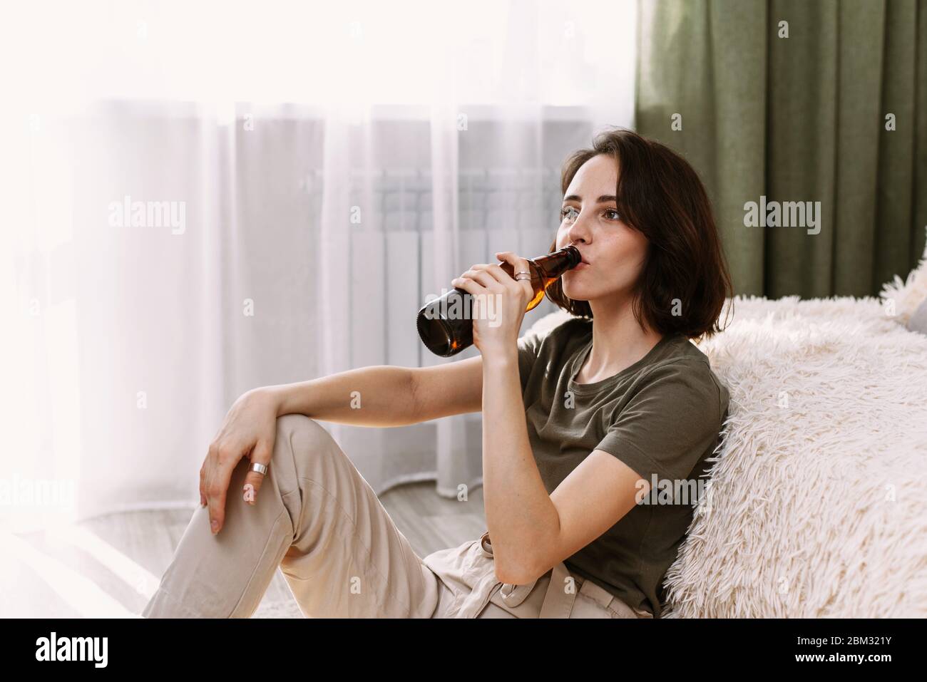 Eine junge Frau trinkt Bier und isst Chips zu Hause. Entspannen Sie sich zu Hause beim Fernsehen und Filmen. Stockfoto