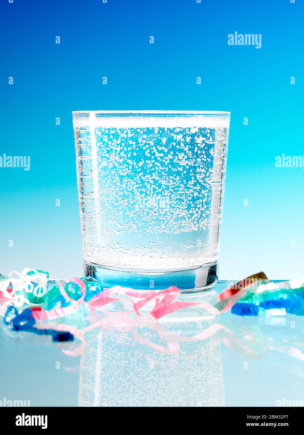 Aufnahme eines Glases Mineralwasser auf blauem Hintergrund mit buntem Band auf dem Tisch Stockfoto